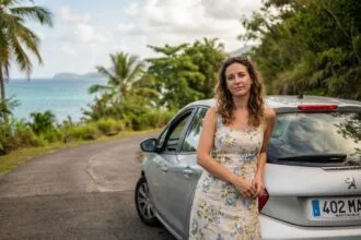 Femme à côté d'une voiture de location sur une route côtière en Martinique entourée de végétation tropicale