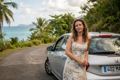 Femme à côté d'une voiture de location sur une route côtière en Martinique entourée de végétation tropicale
