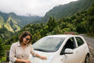 Femme s'appuyant sur une voiture de location sur une route de montagne à La Réunion, consultant une carte avec les cirques volcaniques en arrière-plan