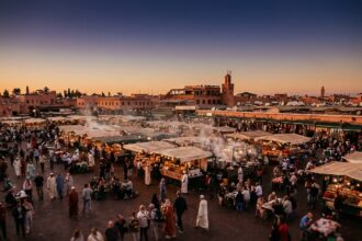 Place Djemaa el-Fna à Marrakech au crépuscule avec étals de nourriture traditionnelle et minaret de la Koutoubia en arrière-plan