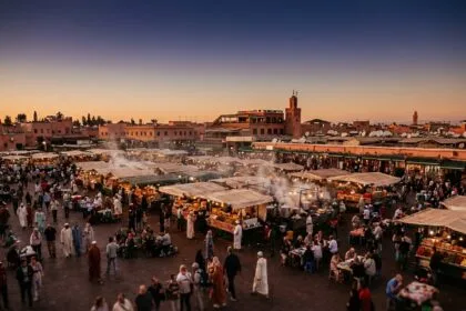 Place Djemaa el-Fna à Marrakech au crépuscule avec étals de nourriture traditionnelle et minaret de la Koutoubia en arrière-plan