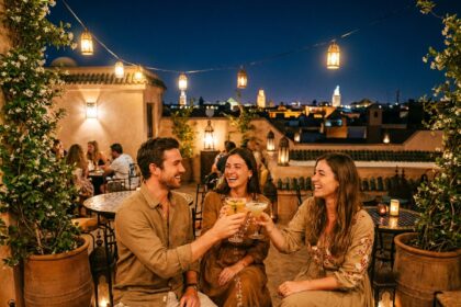 Groupe de jeunes adultes élégants sur un rooftop bar animé à Marrakech la nuit, avec vue sur les toits et les minarets illuminés
